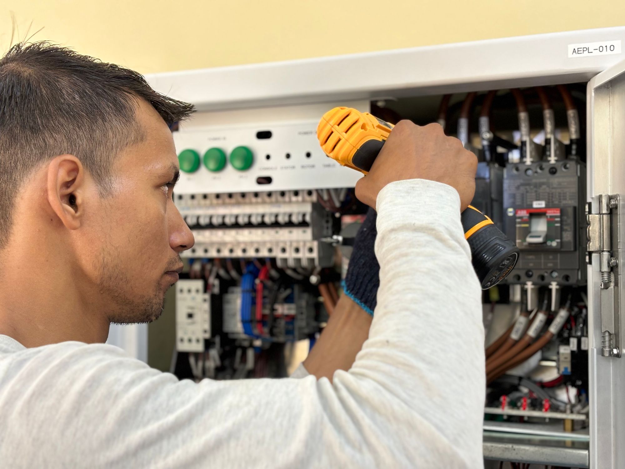 An Ironbark electrician drilling inside an open commercial electrical panel